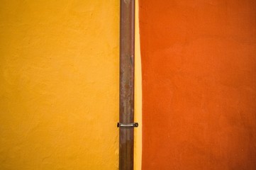 Isolated metallic gutter tube in a red and yellow wall background (Prague, Czech Republic, Europe) 