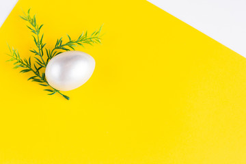 Easter holiday composition. Silver-colored egg with a sprig of greens on a double yellow-white background. Easter flat ley. Easter concept. Copyspace.