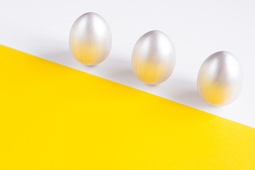 Easter holiday composition. Three eggs of silver color on a double yellow-white background. Easter flat ley. Easter concept. Copyspace.