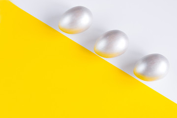 Easter holiday composition. Three eggs of silver color on a double yellow-white background. Easter flat ley. Easter concept. Copyspace.