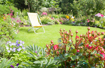 Garden chair on a green lawn in a beautiful flower garden in summer. Shallow dept-of-field, deck...