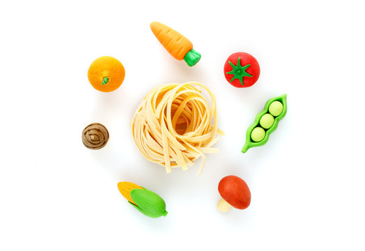 Miniature pasta with vegetables from a platik toy on a white background top view. Creative concept.