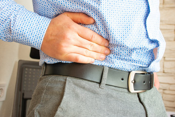 Man holds his hand in area of right lower quadrant of abdomen or bottom of abdomen on right in appendix and colon area due to occurrence of pain. Concept photo of symptoms and signs of appendicitis