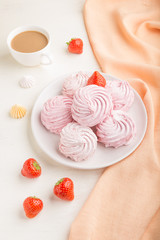 Pink strawberry homemade zephyr or marshmallow with cup of coffee on white wooden background. side view.