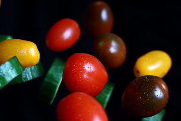multicolored cherry tomatoes with sliced cucumbers in water drops on a dark background