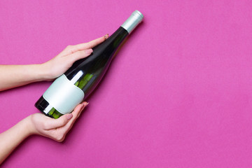 woman hands hold bottle of wine on purple colored paper background top view with copy space