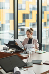 Young businesswoman sitting at conference table and doing paper work before the meeting at office