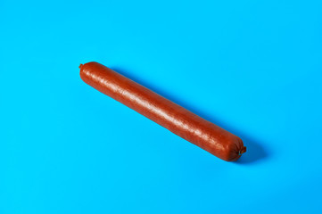 One whole long sausage lies on blue background on kitchen or market. Close-up
