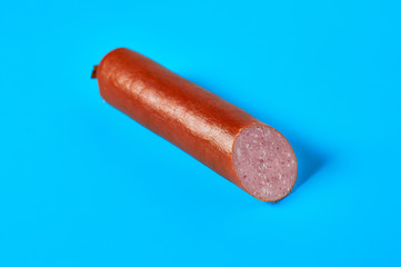 One half of long sausage lies on blue background on kitchen or market. Top view. Close-up