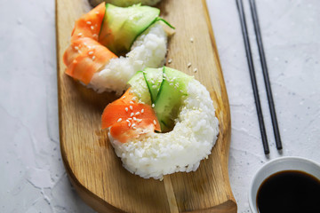 Sushi donuts with raw carrots and cucumber. Vegetarian rice bagel with soy sauce on wooden board. Trendy Japanese food on gray concrete background