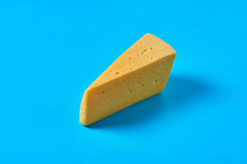 One piece of cheese in form of triangle lies on blue desk on kitchen or market. Close-up