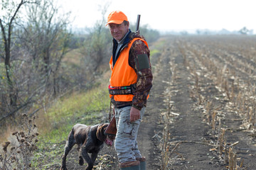 A man with a gun in his hands and an orange vest on a pheasant hunt in a wooded area in cloudy...