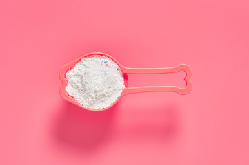 Plastic measuring scoop full of washing powder for cleaning cloth lies on pink countertop in laundry. Top view. Close-up