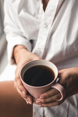 Woman in a white t-shirt holds morning coffee in a pink ceramic cup. Manicure. Front view