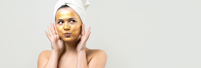 Beauty portrait of woman in white towel on head with gold nourishing mask on face. Skincare cleansing eco organic cosmetic spa relax concept.