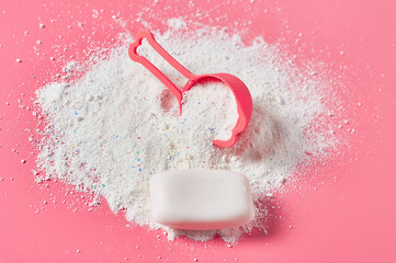 Plastic measuring spoon on heap of washing powder for cleaning clothes and antibacterial soap lies on pink countertop in laundry. Close-up