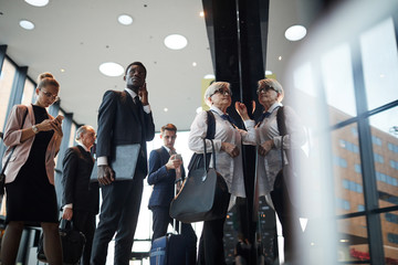 Group of business people with luggage standing in a row and registering at the reception before...