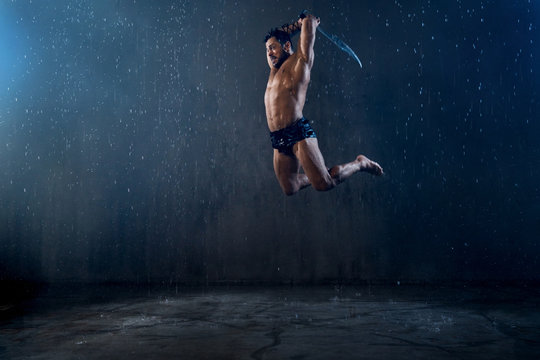 Wet shirtless gladiator jumping in attack.