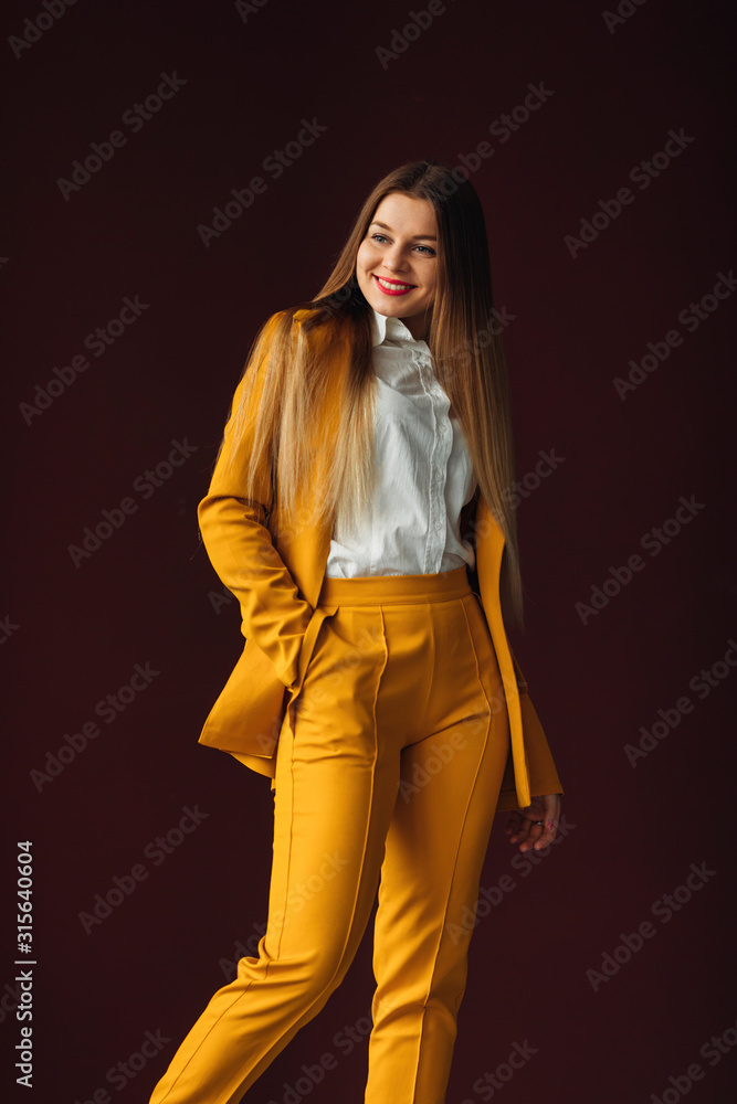 Wall mural beautiful girl in a yellow suit smiles. casual clothes for busin