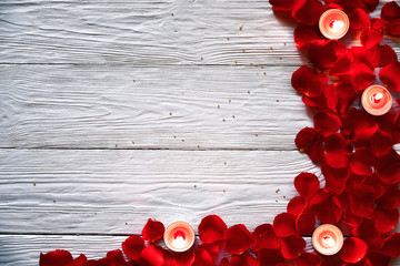 Red rose petals and red burning candles on a white wooden background. St. Valentine's Day background. 