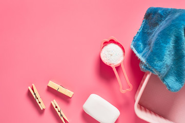 Plastic basket for washing with soft towel near antibacterial soap, clothes pin and measuring spoon full of powder lies on pink countertop in laundry. Space for text. Top view