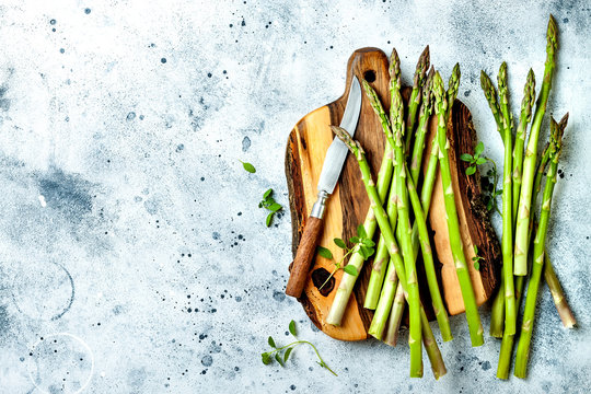 Bunch of fresh green asparagus on wooden board with seasonings. Top view, copy space