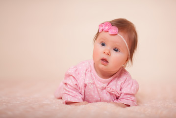 A cute little baby girl with a spring wreath of flowers on her head is very surprised in the Studio in a high key. Concept: baby care, baby food, baby health. Place for the inscription.