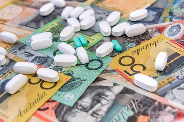 Medicine and cost of health. Dispersed tablets on colorful australian dollar banknotes close up