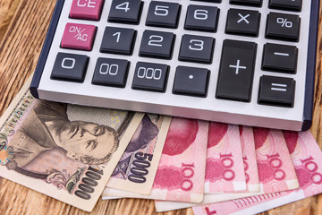 Calculator with chinese and japanese banknotes on wooden background close up