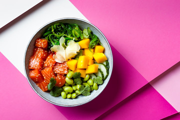 Hawaiian salmon poke bowl with seaweed, avocado, edamame, mango and pickled ginger. Top view, bright pink background