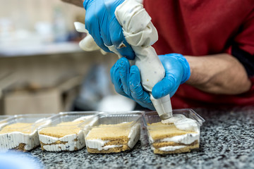 Confector's hands with pastry bag decorating delicious desserts