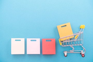 Abstract design element, annual sale, shopping season concept, mini yellow cart with colorful paper bag on pastel blue background, top view, flat lay © RomixImage