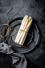 Bunch of fresh white asparagus on vintage metal tray over dark grey rustic background. Top view,...