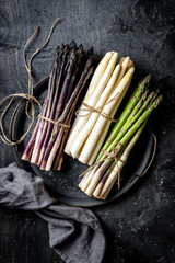Bunches of fresh green, purple, white asparagus on vintage metal tray over dark grey rustic...