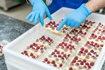 Confectioner decorating delicious desserts with raspberry on factory. Amazing delicious food