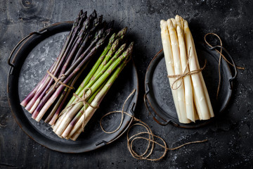 Bunches of fresh green, purple, white asparagus on vintage metal tray over dark grey rustic background. Top view, copy space - Powered by Adobe