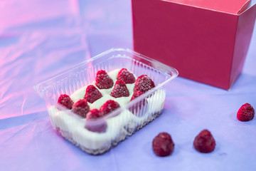 Delicious dessert in plastic package with raspberry on table and pink wrapping close up. Food concept