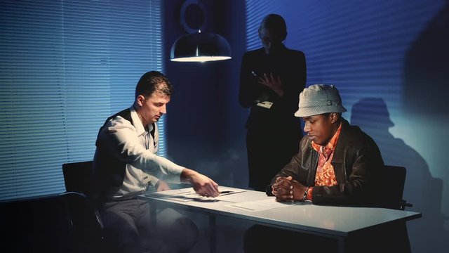 Suspected mixed-race man signing a document of accusation. Interrogation room in smoke.