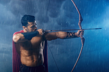 Muscular spartan in red cloak shooting from bow.