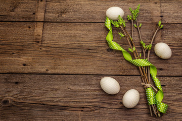 Fototapeta na wymiar Zero waste Easter concept. Spring twigs with fresh green leaves, wooden eggs, polka dot ribbon. Old vintage wooden boards background