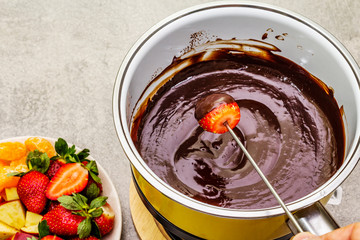 Chocolate fondue. Assorted fresh fruits, two types of chocolate, male hand. Ingredients for cooking a sweet romantic dessert. Stone concrete background