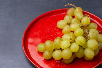 Top view of bunch of green grapes with water drops, on red plate and dark background, with selective focus, horizontally, in Madrid, Spain, Europe