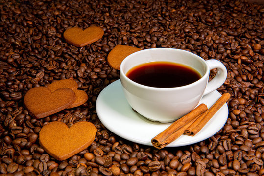White coffee mug,  cinnamon sticks and heart-shaped gingerbread cookies on the coffee beans background - image