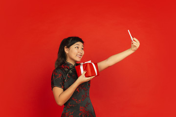 Taking selfie with gift. Happy Chinese New Year 2020. Asian young girl's portrait isolated on red background. Female model in traditional clothes looks happy. Celebration, holiday, emotions. Copyspace