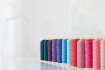 Row of multicolored spools of sewing threads on a white table. Workplace of seamstress. Sewing background with copy space