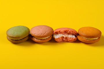 colorful macaroons with one piece half eaten on yellow background