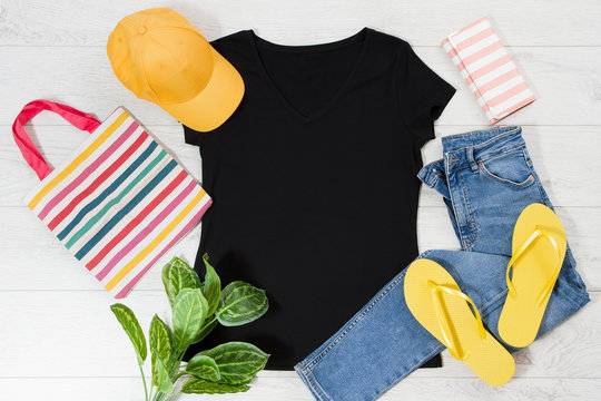 T shirt black and slippers. T-shirt Mockup flat lay with summer accessories. Hat, bag, yellow flip flops on wooden floor background. Copy space. Template blank canvas. Front top view.