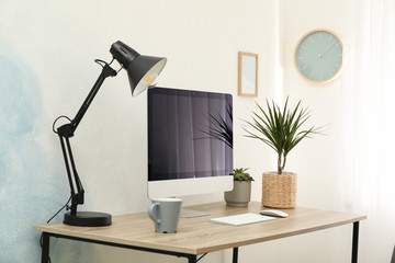 Workplace with computer, plants and lamp on wooden table. Empty black screen