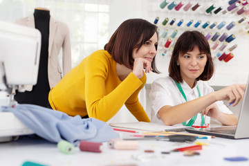 Fototapeta premium Two young female dressmakers working in sewing studio. Sisters start family business. Bespoke tailoring. Private enterprise. Hobby and business
