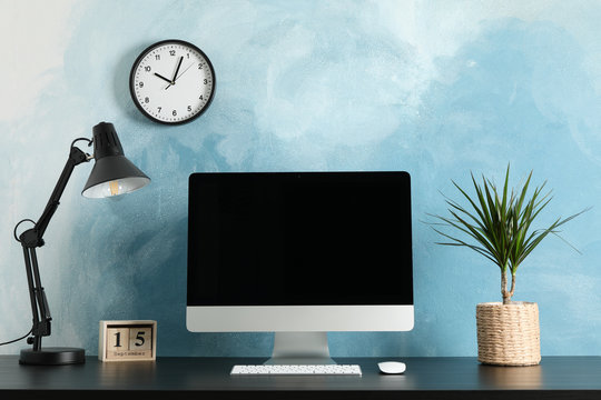 Workplace with computer, plant and lamp on wooden table. Light blue background